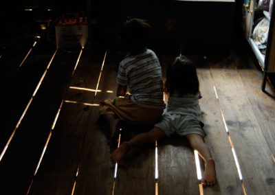 Enfants regardant la télé, allongés au sol dans leur maison, village de Sra Srang, province de Siem Reap.